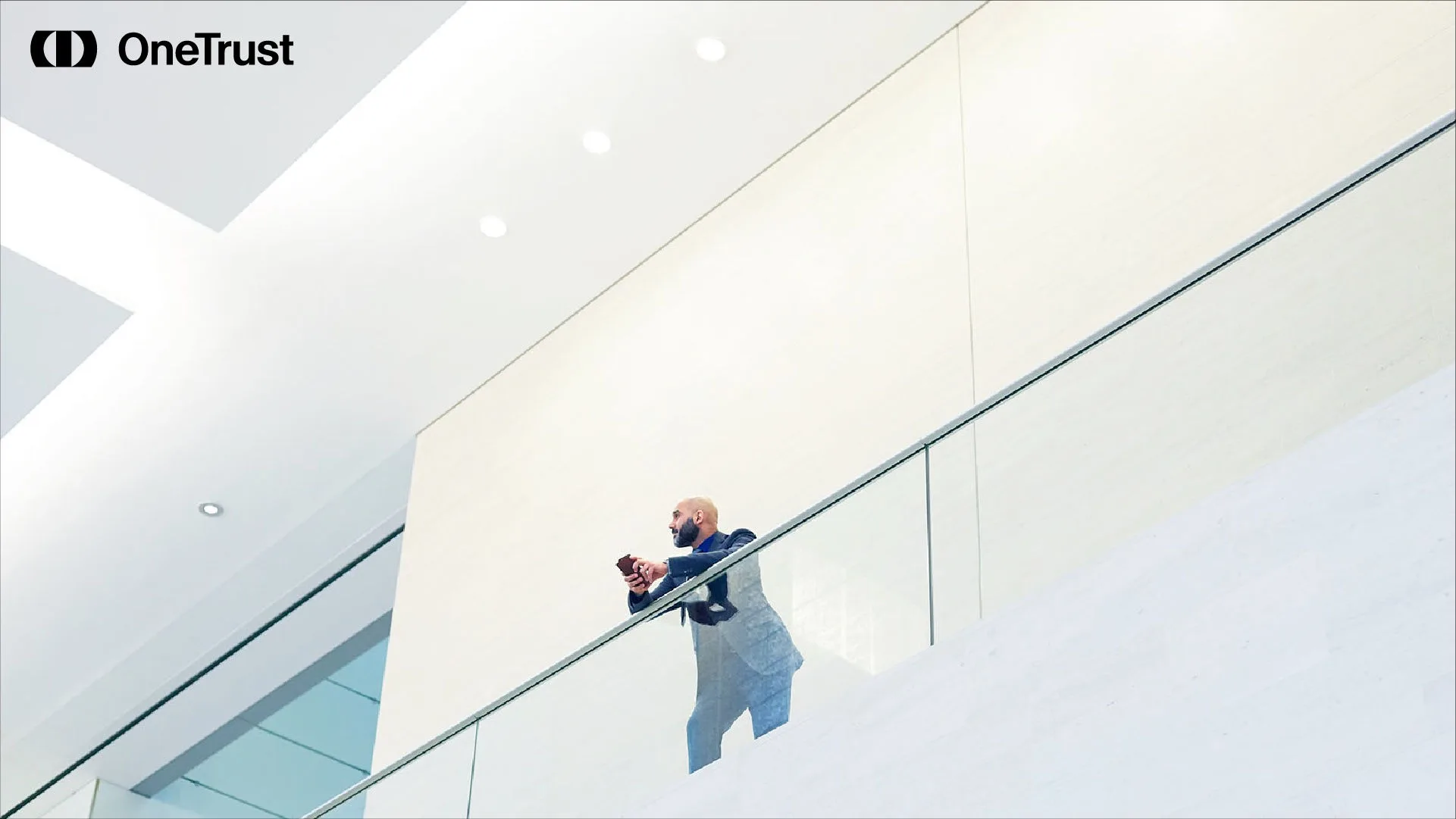 Person standing on a modern office balcony using a mobile device, with the OneTrust logo visible, representing digital governance and AI compliance planning.