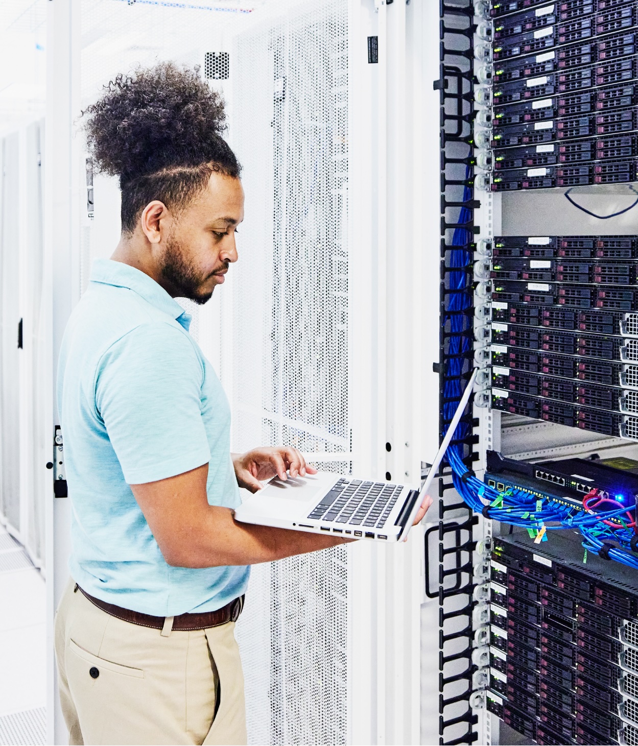 IT worker examines a server rack with his MacBook.