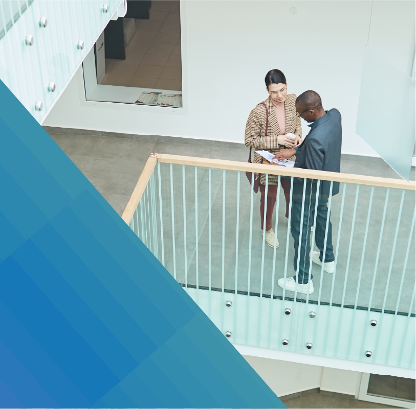 Two people in business attire discuss a project on an indoor office balcony