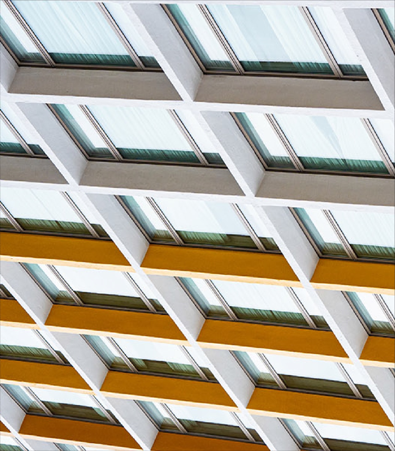 A repeating architectural pattern of angled glass windows and white structural beams.